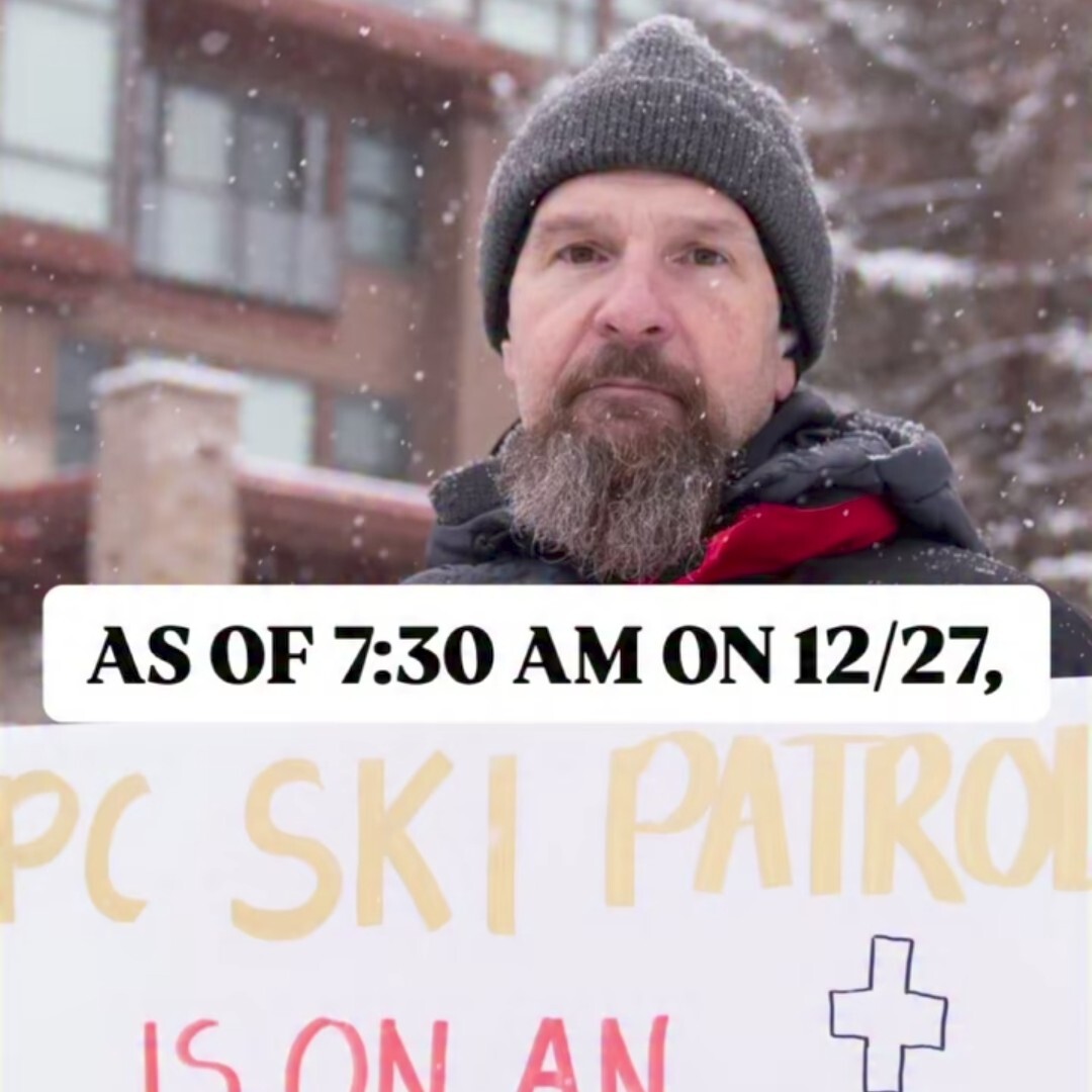 a ski patroller holding a sign that says "PC ski patrol is on[cutoff]"