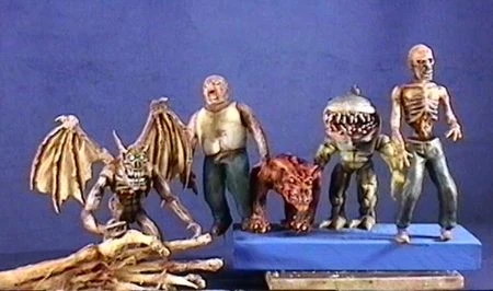 Production photo of the real world models sculpted and digitally captured for the game Blood (1996).  From left to right the creatures are as follows. A Gargoyle held by a skeletal hand, then a Fat Zombie, HellHound, Gill Beast, and Zombie, all standing on a blue platform.