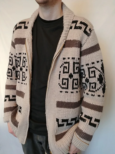A person modeling a knit cardigan in the famous Cowichan style cardigan in a beige colors with brown stripes and black spiraly designs