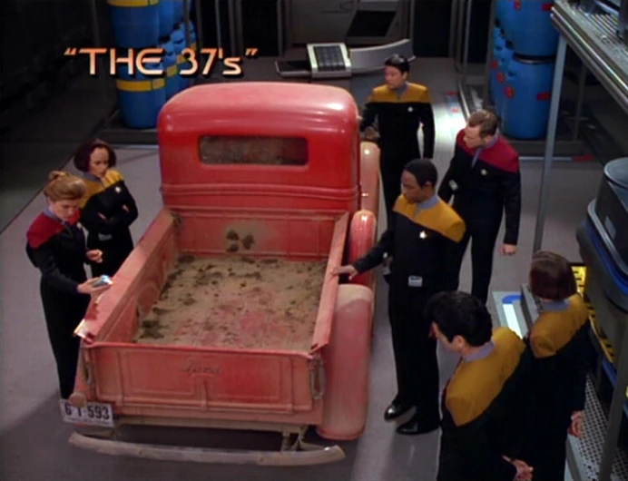 Title card from Star Trek: Voyager S02E01, with the crew of Voyager standing around a 1936 Ford truck in their cargo bay. The episode title "The 37's" is at the top left of the image.