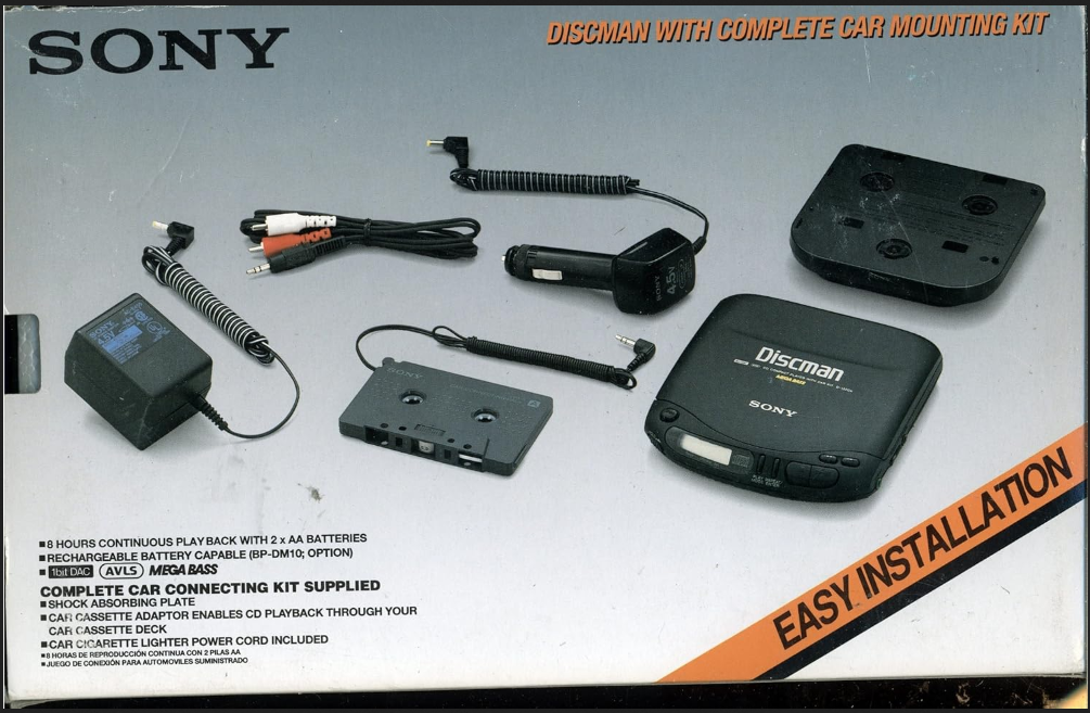 photo of a cardboard box packaging for SONY DISCMAN WITH COMPLETE CAR MOUNTING KITpackage has this text on top of a photo of the discman and accessories listed:8 HOURS CONTINUOUS PLAY BACK WITH 2 x AA BATTERIESRECHARGEABLE BATTERY CAPABLE (BP-DM10; OPTION)1bit DAC AVLS MEGABASSCOMPLETE CAR CONNECTING KIT SUPPLIEDSHOCK ABSORBING PLATECAR CASSETTE ADAPTOR ENABLES CD PLAYBACK THROUGH YOURCAR CASSETTE DECKCAR CIGARETTE LIGHTER POWER CORD INCLUDEDbeneath the English-language text is this smaller text in Spanish:8 HORAS DE REPRODUCCIÓN CONTINUA CON 2 PILAS AAJUEGO DE CONEXIÓN PARA AUTOMOVILES SUMINISTRADOacross the bottom right corner it says:EASY INSTALLATION