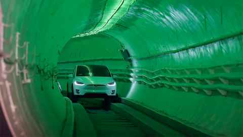 photo of one of elon musk's shit tunnels with a tesla on a track, lit up with rgb tunnel lights set to green