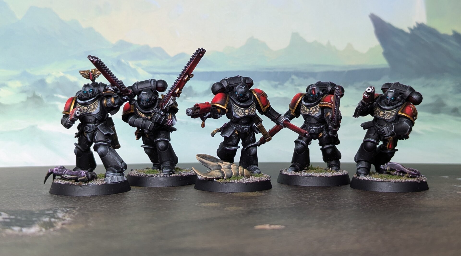 A photograph of five painted Warhammer 40,000 miniatures. Black power armor with red and gold accents.