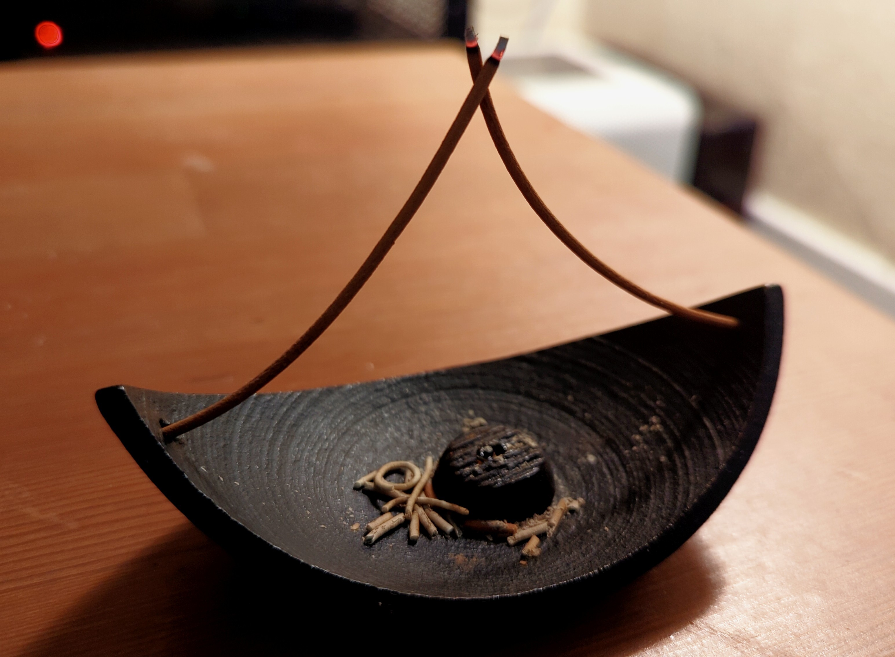 Two very curved coreless incense sticks, each inserted into opposite ends of a cast iron burner. They come together to form a point.