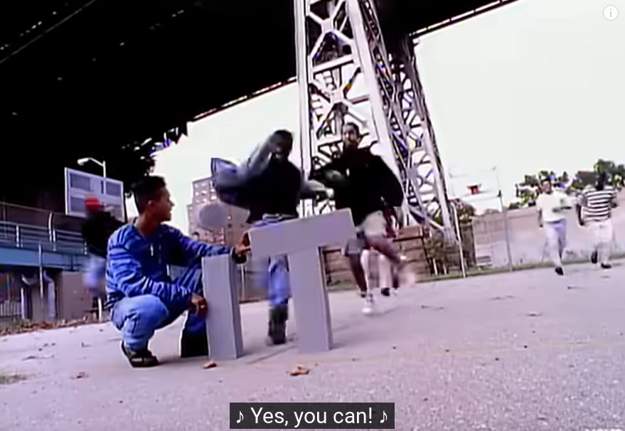 screenshot of the moment at 2:07 in "A Tribe Called Quest - Can I Kick It? (Official HD Video)" when the letters "iT" are about to be kicked over, with the subtitle "♪ Yes, you can! ♪" at the bottom of the frame